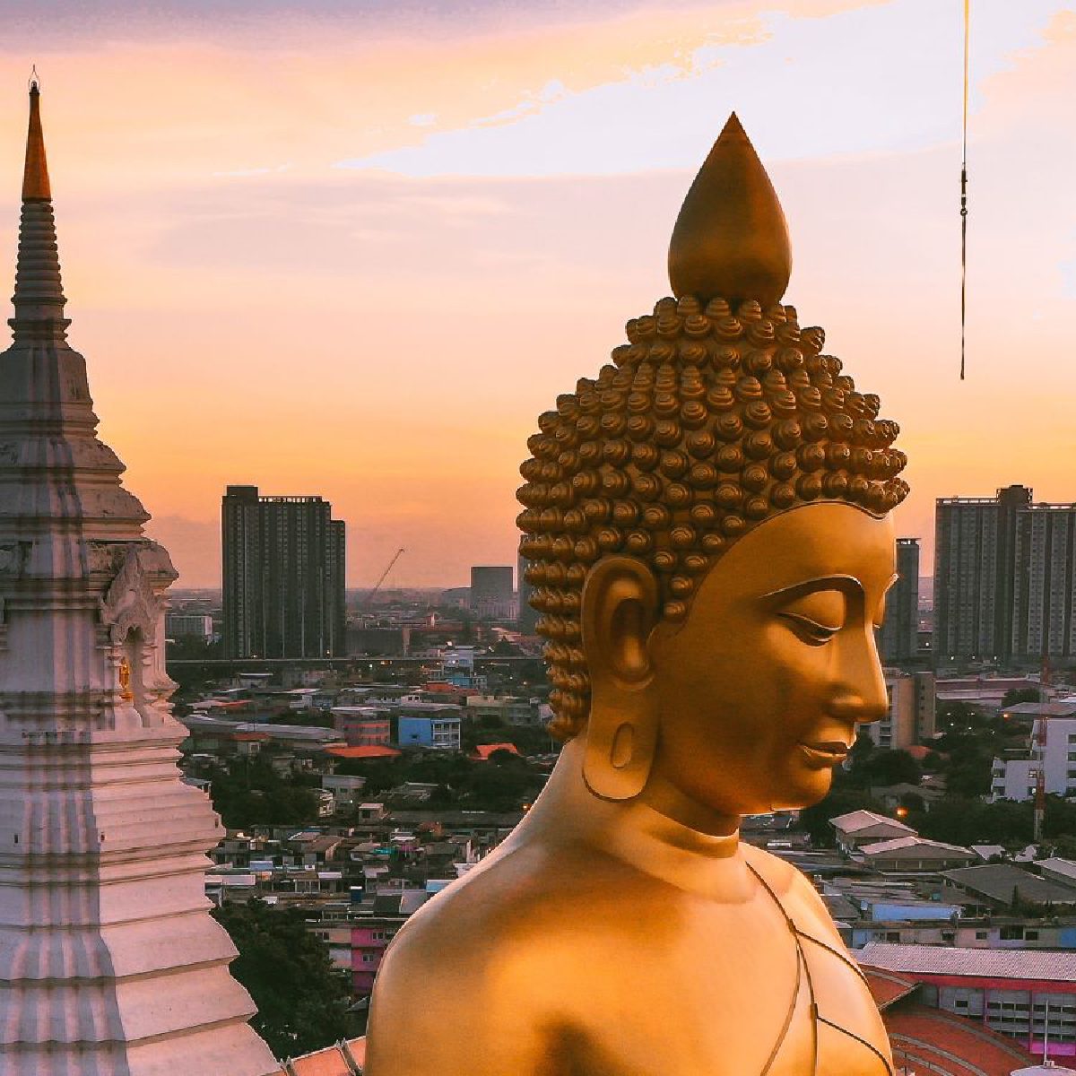 Un Bouddha doré et un chedi au coucher du soleil, les tours de Bangkok en arrière-plan